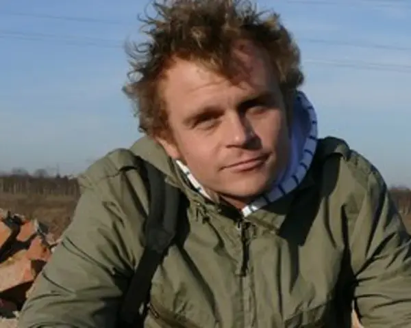 Piotr Rogucki, w otoczeniu gruzu, z charakterystyczną fryzurą, jakby inspirowany swoimi utworami.