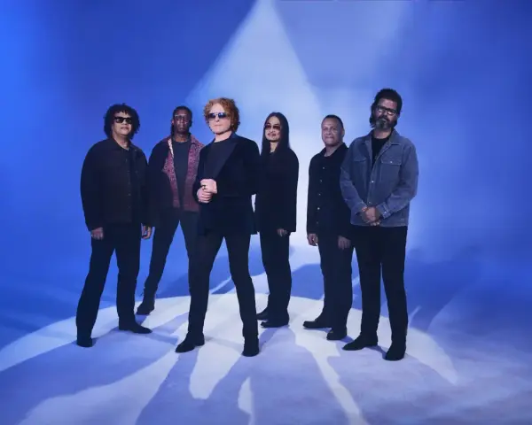 Zespół Simply Red gotowy na koncert w Polsce. Sześciu muzyków pozuje na tle niebieskiego światła.