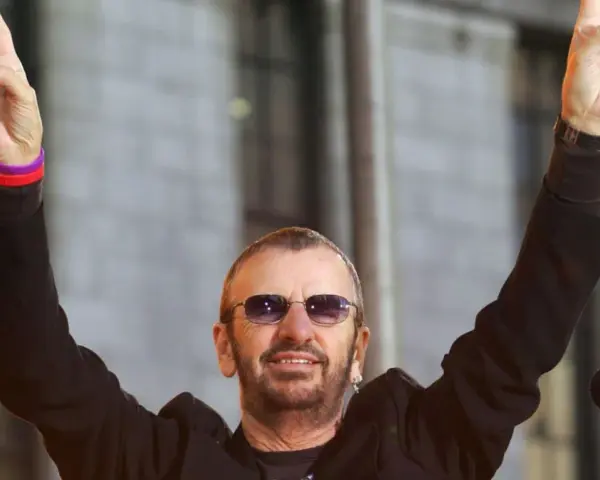 Ringo Starr z The Beatles pozdrawia fanów, unosząc ręce w geście pokoju.