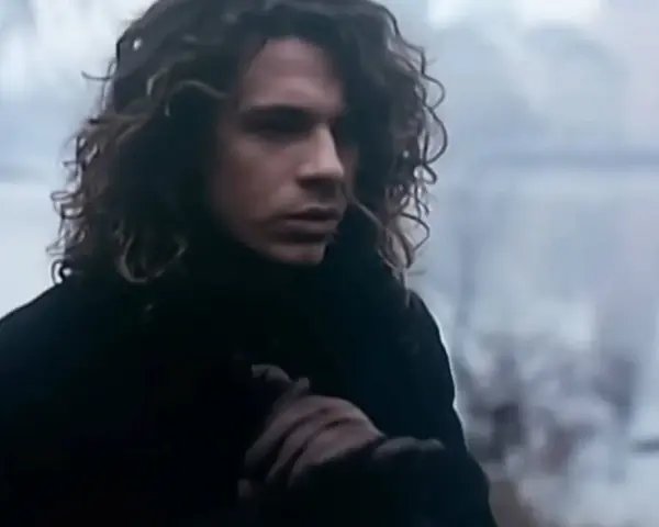 Mężczyzna z kręconymi włosami w czarnym płaszczu, trzymający się za rękę, jakby chciał powiedzieć "never tear us apart".