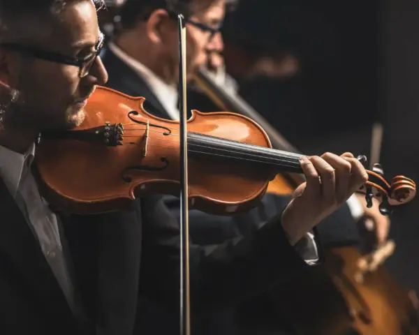 Skrzypek grający melodię, która mogłaby być jedną z piosenek o Krakowie. W tle inni muzycy orkiestry.