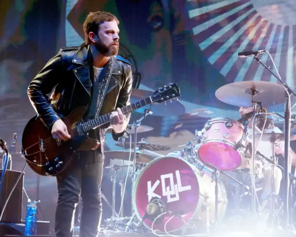 Gitarzysta Kings of Leon Polska w skórzanej kurtce gra na scenie. W tle perkusja z logo KQL.