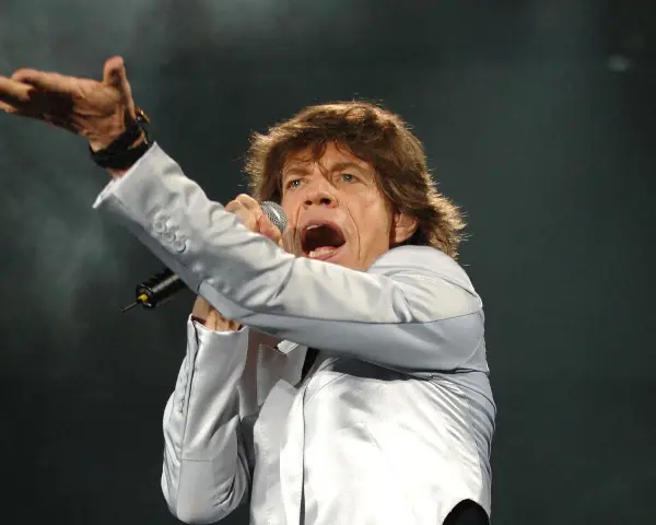 Mick Jagger, wokalista zespołu, śpiewa z mikrofonem, gestykulując ręką.