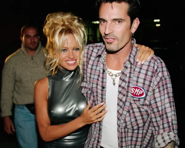 Pamela Anderson i Tommy Lee, ikony lat 90., pozują do zdjęć. Pamela w błyszczącej sukience, Tommy w kratowanej koszuli.