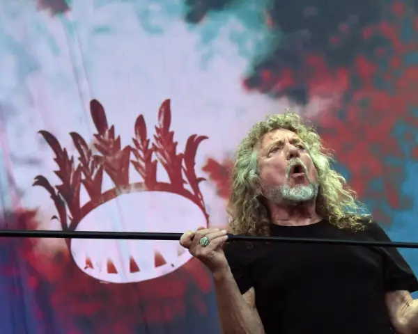 Wokalista Led Zeppelin, Robert Plant, śpiewa z pasją na tle scenografii z koroną.