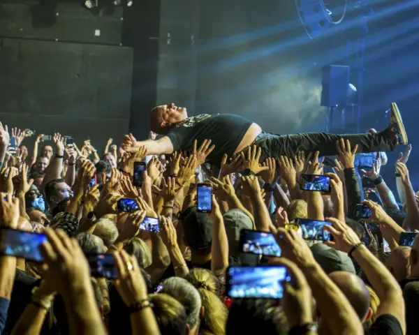 Kult w Arahji: wokalista zespołu niesiony przez tłum, fani nagrywają koncert telefonami.