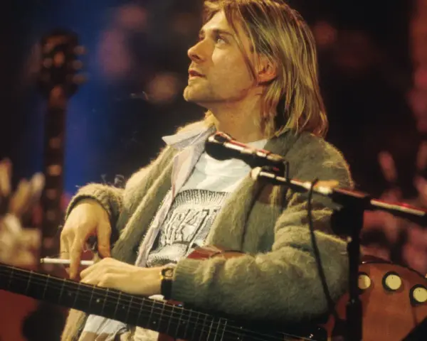 Kurt Cobain z papierosem w dłoni, grający na gitarze. Jego muzyka to część 100 najlepszych piosenek wszechczasów.