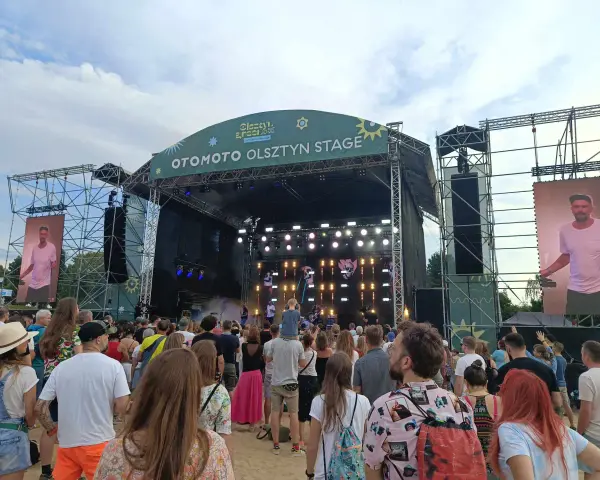 Tłum na festiwalu, na scenie OTOMOTO OLSZTYN STAGE. Kim Nowak w piasku, wśród ludzi.
