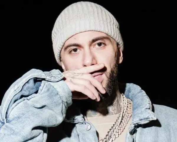 Malik Montana w czapce i jeansowej kurtce, z dłonią na ustach, gotowy na koncert.