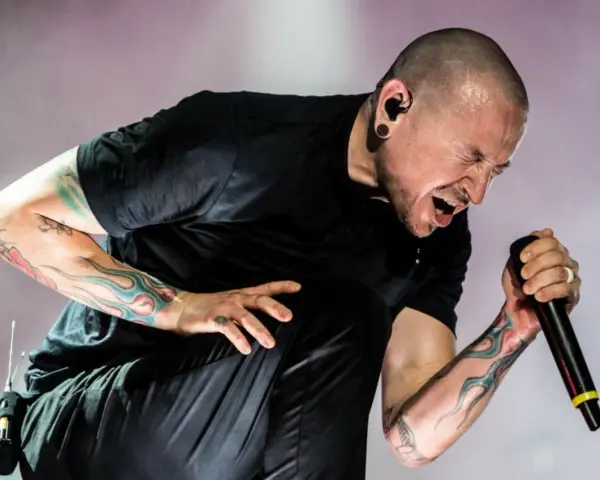 Chester Bennington z Linkin Park, z tatuażami na ramionach, śpiewa do mikrofonu z pasją.