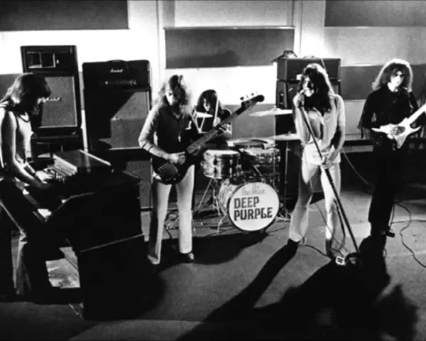 Zespół Deep Purple w akcji. Muzycy grają na instrumentach, w tle perkusja z logo zespołu.