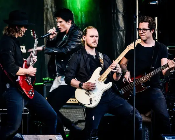 Zespół gra na scenie, wokalista śpiewa, gitarzyści i basista tworzą muzykę. Może to piosenka "Kocham Cię".