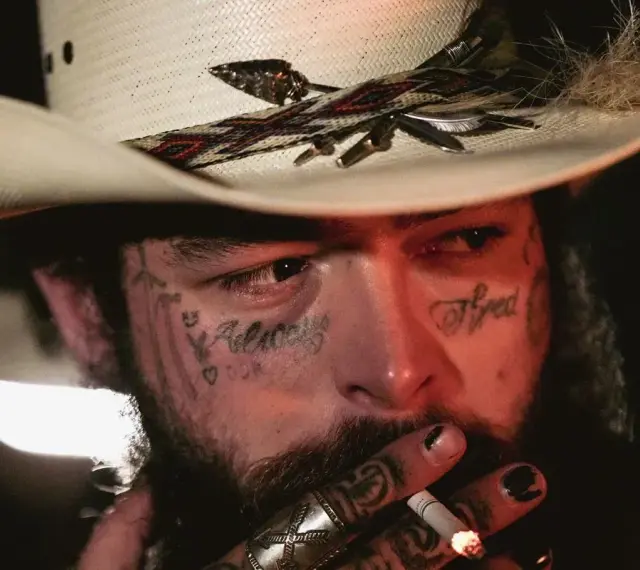 Post Malone w kapeluszu kowbojskim, z tatuażami na twarzy, pali papierosa. Jeden z najsłynniejszych wykonawców muzyki country.