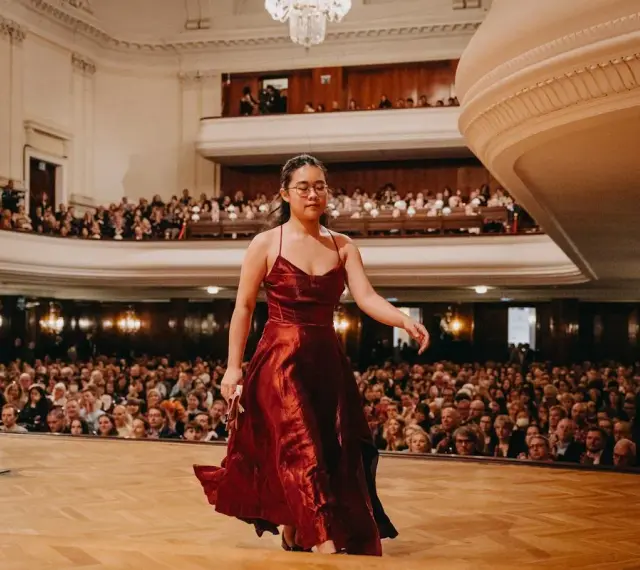 Młoda pianistka w czerwonej sukni wchodzi na scenę, by wykonać nokturn. Publiczność w teatrze czeka na występ.