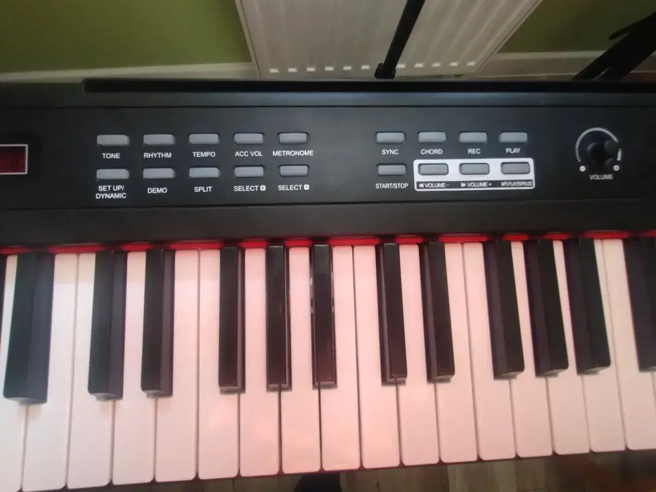 Czarny keyboard z białymi i czarnymi klawiszami. Na panelu sterowania widoczne są przyciski z napisami, np. 