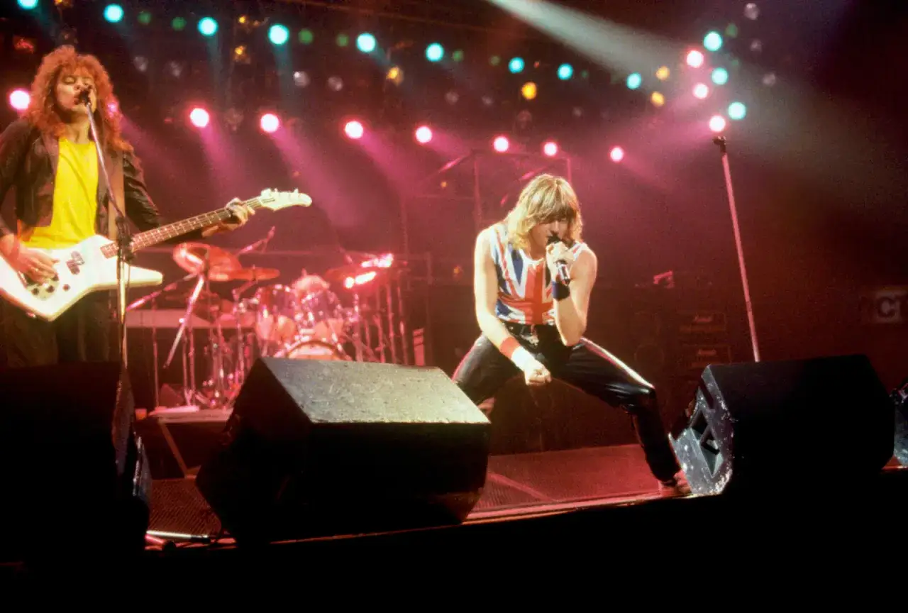 Joe Elliott śpiewa na scenie, a Rick Savage gra na basie. Koncert zespołu Def Leppard, znany z energetycznych utworów.