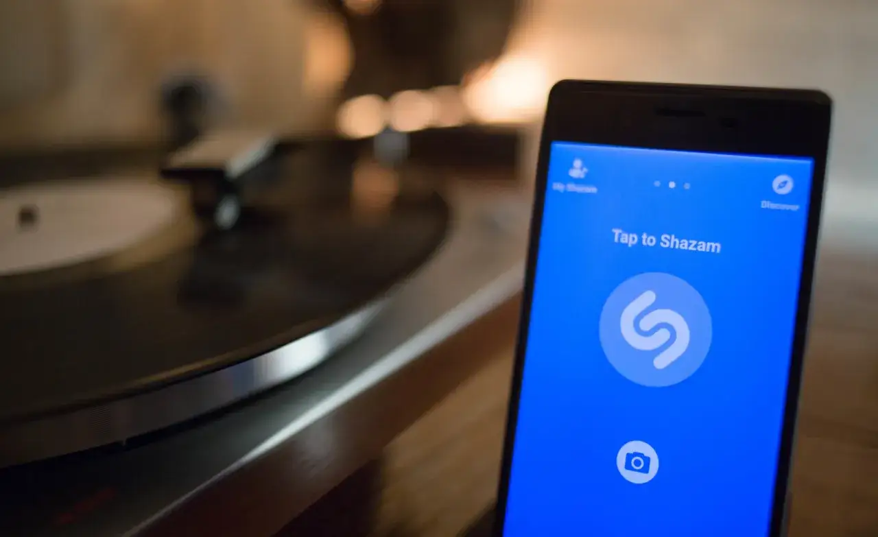 Telefon z aplikacją Shazam obok gramofonu. Dowiedz się, jak znaleźć tytuł piosenki po fragmencie, używając tej aplikacji.