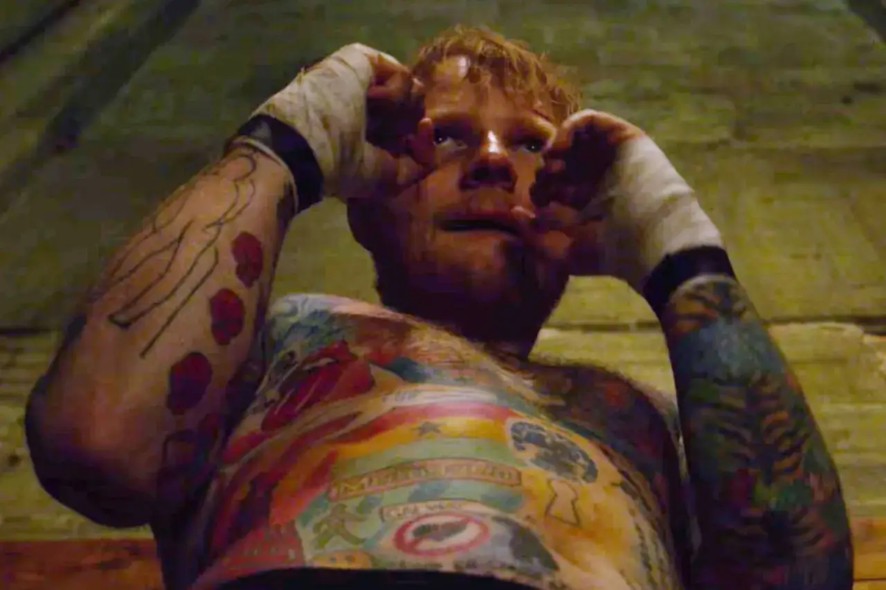 Ed Sheeran z kolorowymi tatuażami na torsie i ramionach, z bandażami na nadgarstkach.