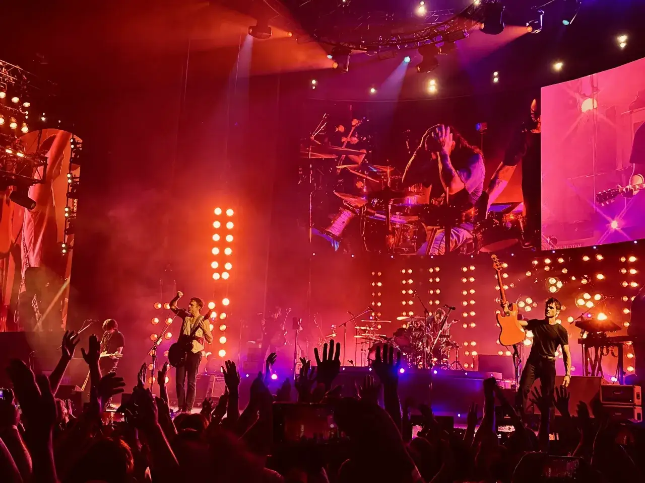 Koncert Kings of Leon w Polsce. Energetyczny występ zespołu na tle czerwonych świateł i ekranów.