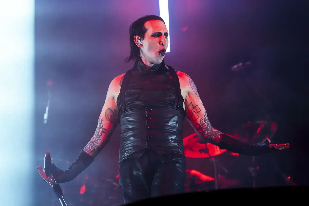 Marilyn Manson na koncercie w Warszawie, w skórzanym stroju, z mikrofonem w dłoni.