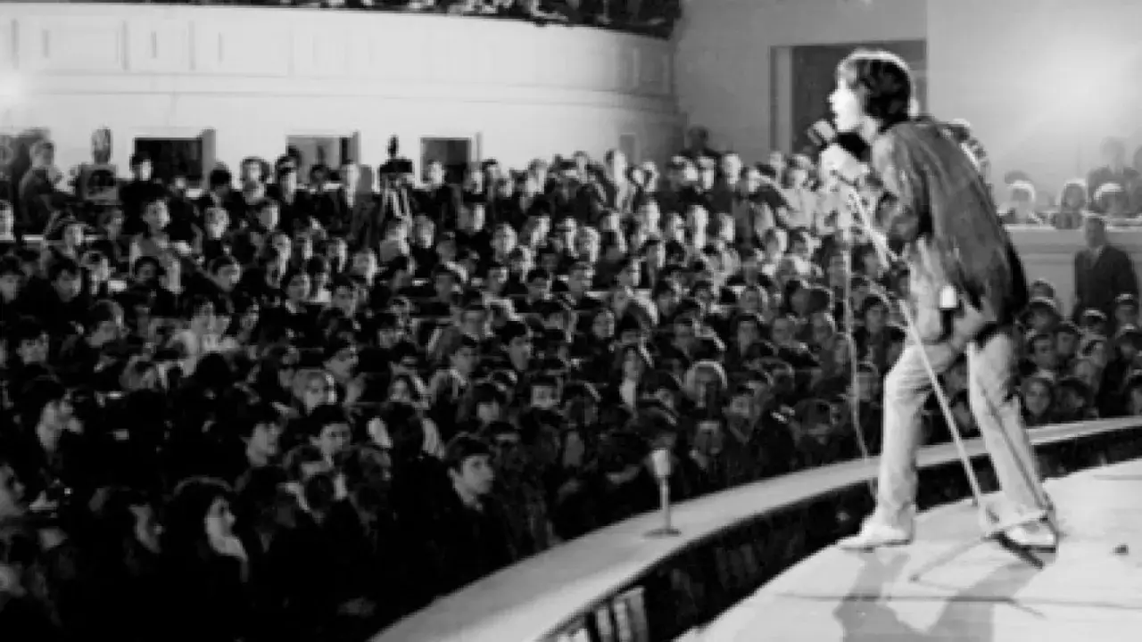 Mick Jagger śpiewa na jednym z pierwszych koncertów Rolling Stones. Tłum fanów wpatrzony w scenę.