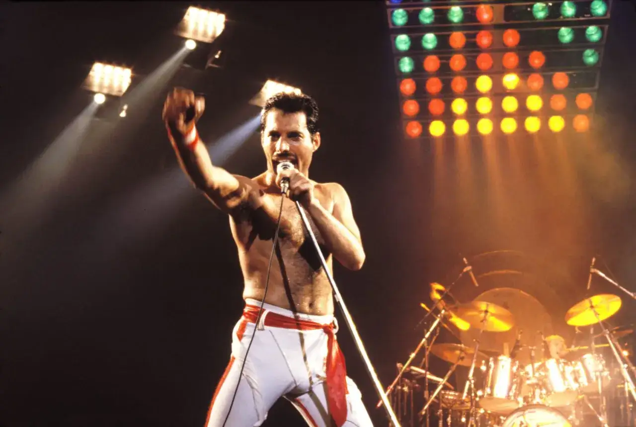 Freddie Mercury śpiewa na scenie, wznosząc pięść. To może być jego ostatnia piosenka Queen, pełna energii i pasji.
