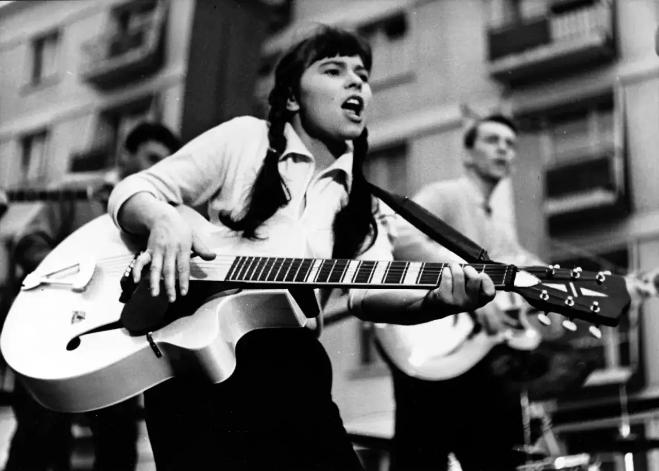 Karin Stanek śpiewa i gra na gitarze, w tle widać innych muzyków.