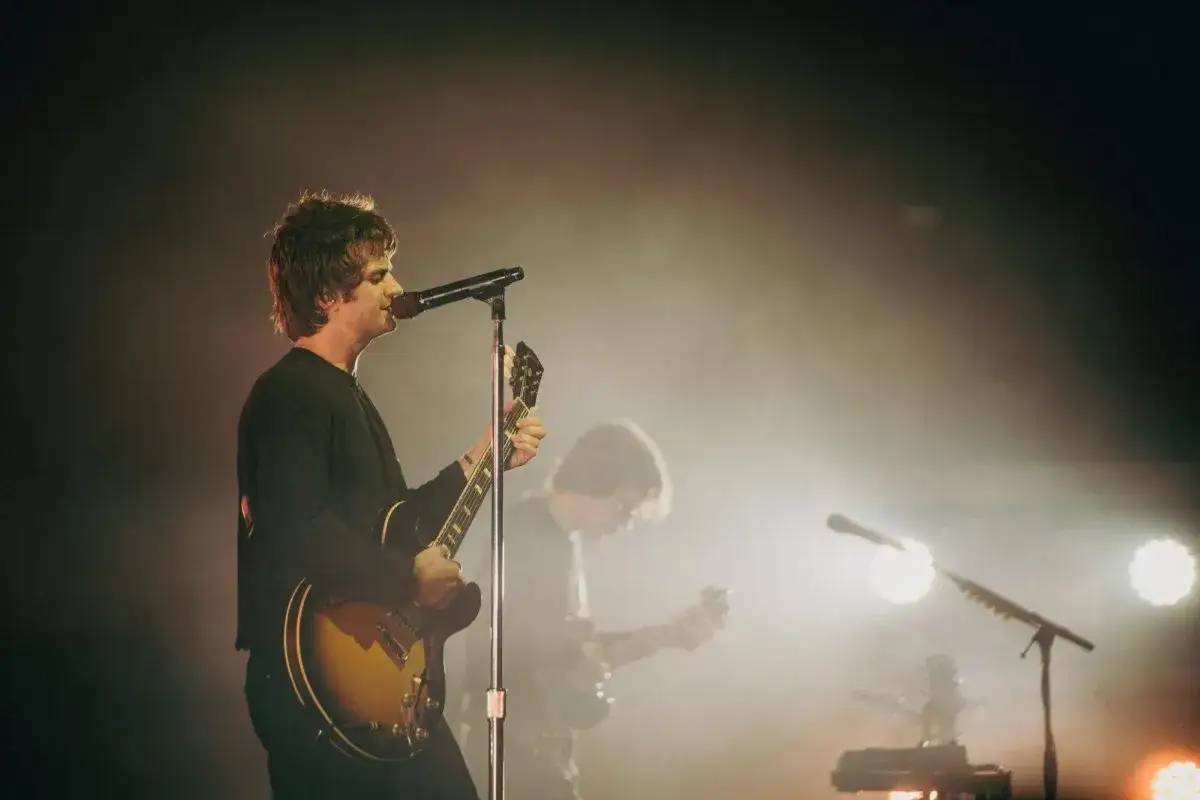 Joe Keery gra na gitarze i śpiewa na scenie, otoczony mgłą i światłami.