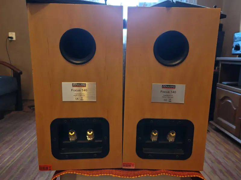 Dwa głośniki Dynaudio Focus 140 w drewnianej obudowie, z widocznymi złączami i tabliczkami znamionowymi.