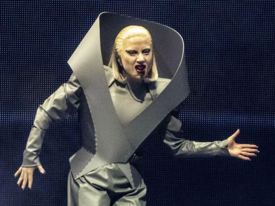 Lady Gaga w Polsce w futurystycznym stroju, z charakterystycznym makijażem i uniesioną ręką.